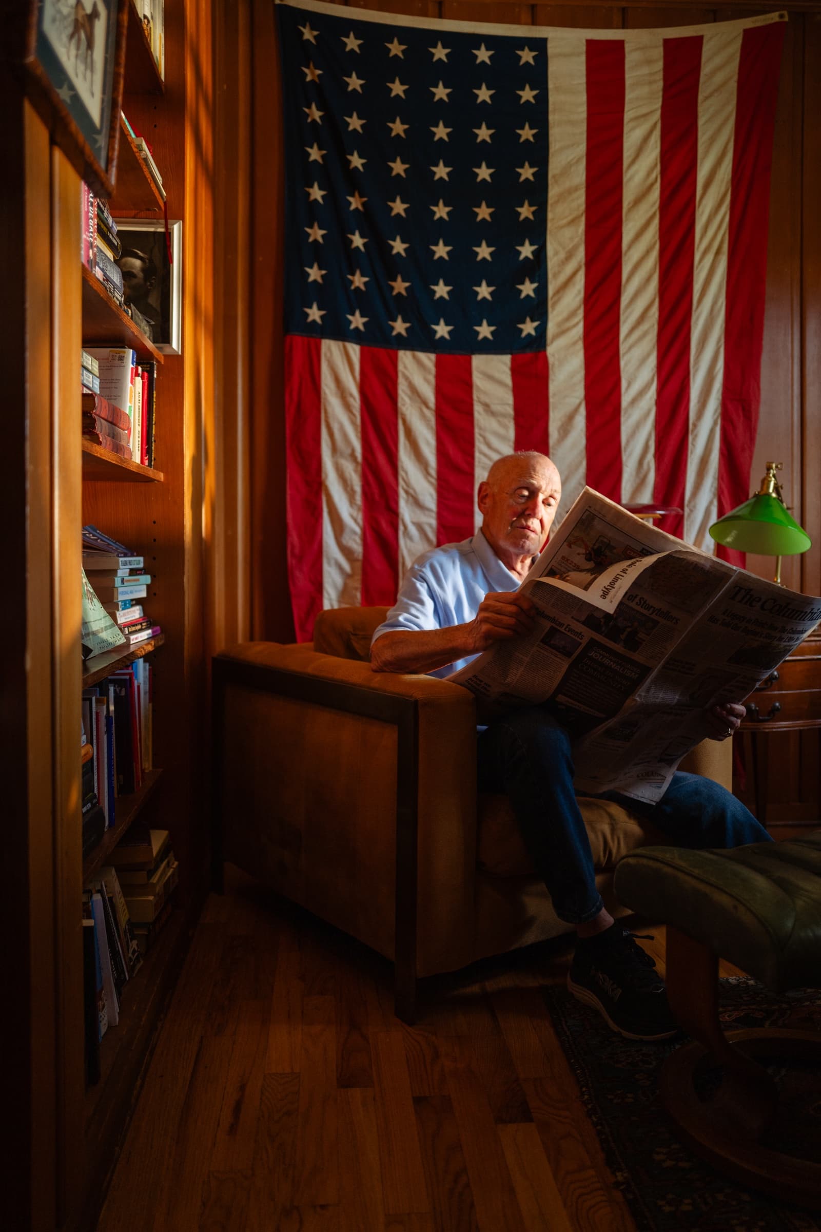 Man reading The Columbian in study with American flag