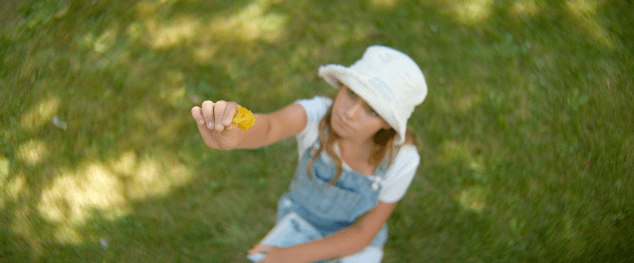 Girl in overalls holding something up toward camera